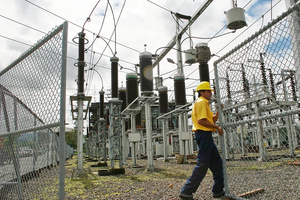 Un ouvrier d'entretien ouvre la porte de clôture à mailles de chaîne pour l'inspection des installations électriques.