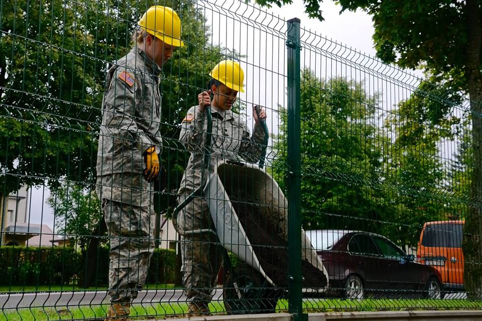 Deux soldats chargent du béton pour la construction de clôtures militaires soudées sinueuses.