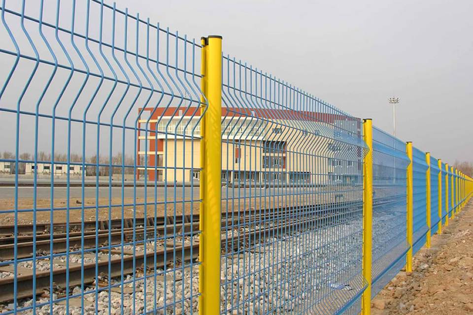 Las vías del tren y una sala de oficinas están rodeadas por una valla soldada con curvas.