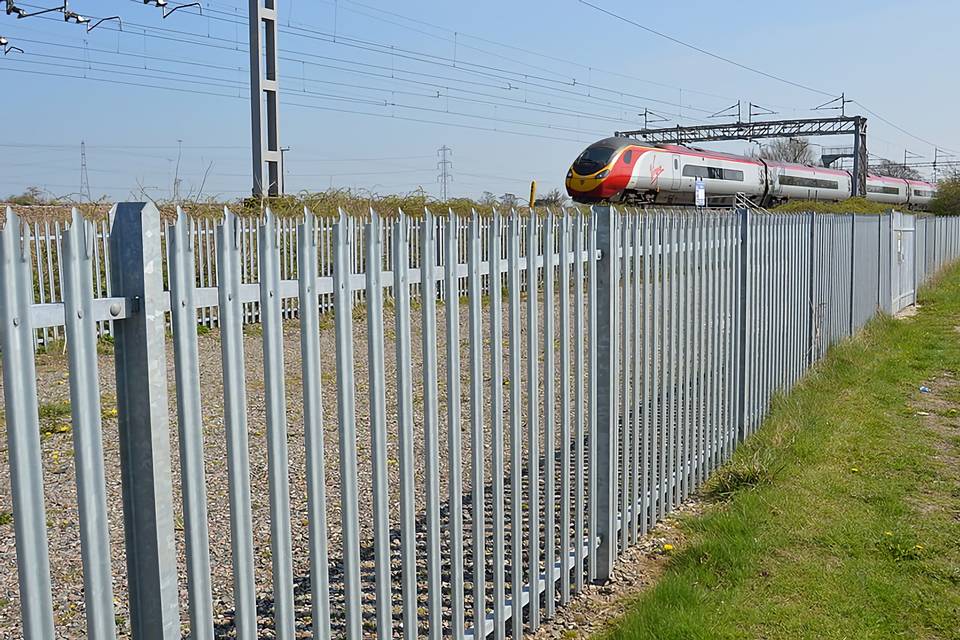 Un tren circula por la vía del tren rodeada por vallas empalizadas.