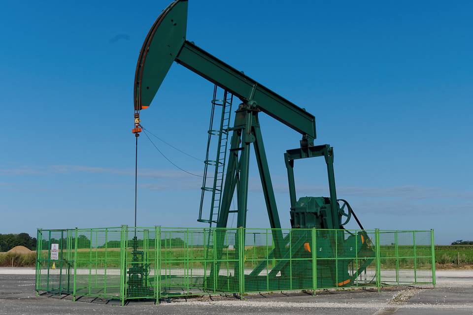 Un conjunto de máquinas de desarrollo de aceite está estacionando en la cerca del campo petrolífero hecha de paneles de malla de alambre soldados.